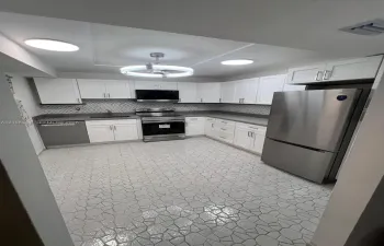 Kitchen featuring white shaker-style cabinetry, stainless steel appliances, patterned tile backsplash, solid-surface countertops, and geometric tile flooring