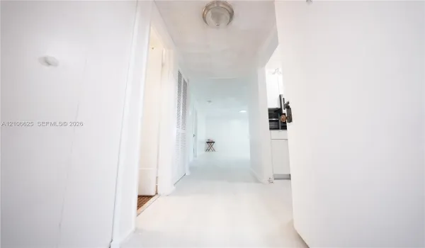 Hallway featuring white hard-surface flooring, louvered closet doors, and a flush-mount ceiling light fixture