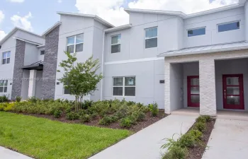 Contemporary exterior featuring multi-textured facade with grey paneling and stone veneer accents, shed-style rooflines, and bold red-toned front entry doors