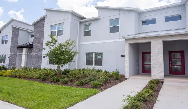 Contemporary exterior featuring multi-textured facade with grey paneling and stone veneer accents, shed-style rooflines, and bold red-toned front entry doors