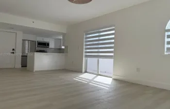 Open-concept kitchen featuring stainless steel appliances, white cabinetry, and a peninsula, complemented by wood-finish flooring and dual-tone window shades