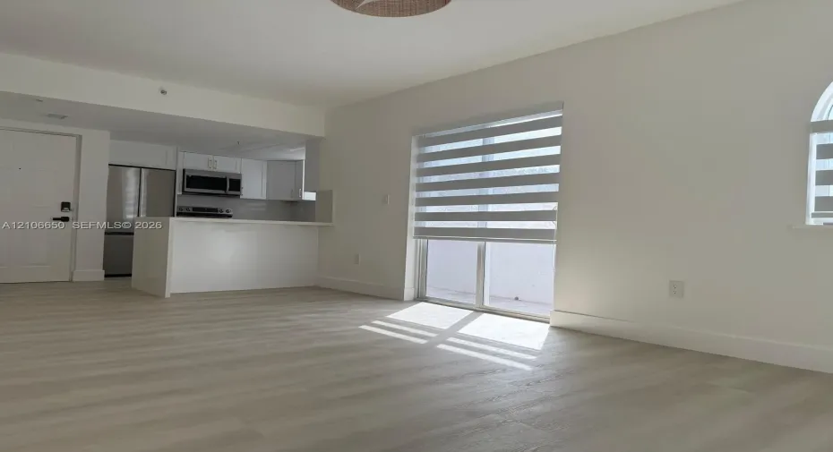 Open-concept kitchen featuring stainless steel appliances, white cabinetry, and a peninsula, complemented by wood-finish flooring and dual-tone window shades