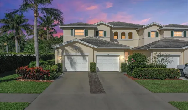 Stucco exterior featuring two garage bays, concrete driveway, arched window detailing, and manicured landscaping