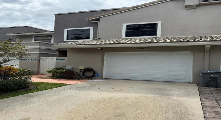 Two-story stucco exterior featuring a concrete tile roof, single-car garage with a sectional door, and an integrated private gated entrance