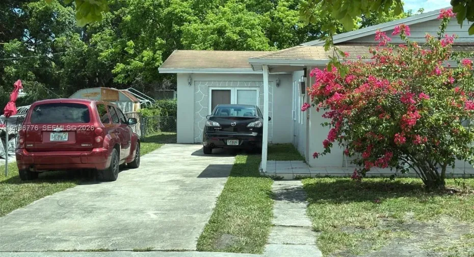 Single-story exterior featuring light-toned masonry, a concrete driveway, a covered front entry, and mature landscaping