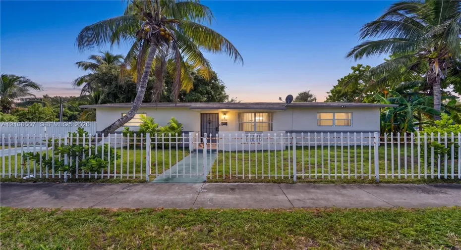 Single-story residence featuring a painted exterior, front porch, white metal perimeter fencing, concrete walkway, and mature landscaping