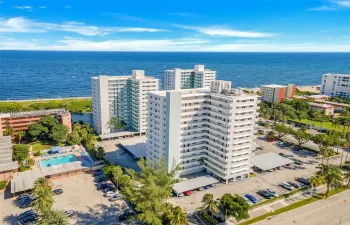 High-rise residential building featuring expansive oceanfront positioning, dedicated swimming pool, covered parking structures, and manicured tropical landscaping
