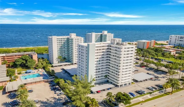 High-rise residential building featuring expansive oceanfront positioning, dedicated swimming pool, covered parking structures, and manicured tropical landscaping