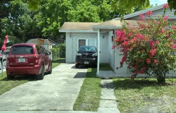 Single-story exterior featuring light-toned masonry, a concrete driveway, a covered front entry, and mature landscaping