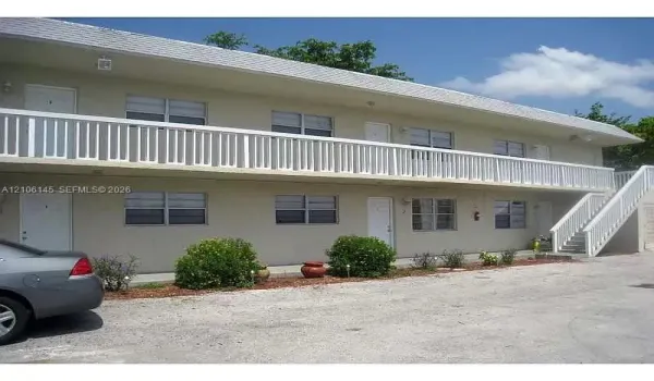 Two-story exterior featuring a white picket-style balcony railing, concrete staircase, neutral stucco facade, and multi-pane windows