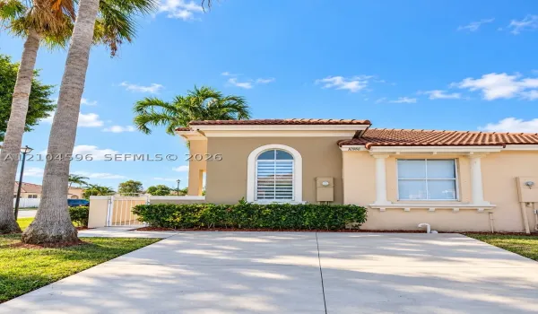 Stucco exterior featuring a terracotta tile roof, arched window with decorative trim, and metal gated side entry