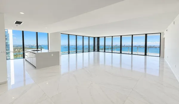 Open-concept space featuring floor-to-ceiling windows, polished stone-finish tile flooring, and a kitchen island with a neutral countertop and integrated sink