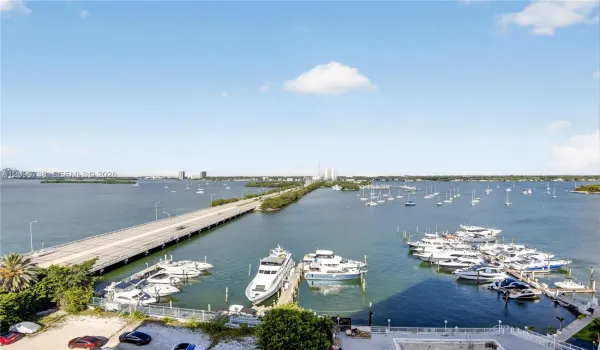 Waterfront setting featuring a private marina with multiple deep-water slips, paved causeway access, and panoramic coastal horizon