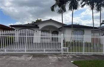 Single-story residence featuring a gated entry, arched front porch, tile roof, arched windows, and mature palm trees