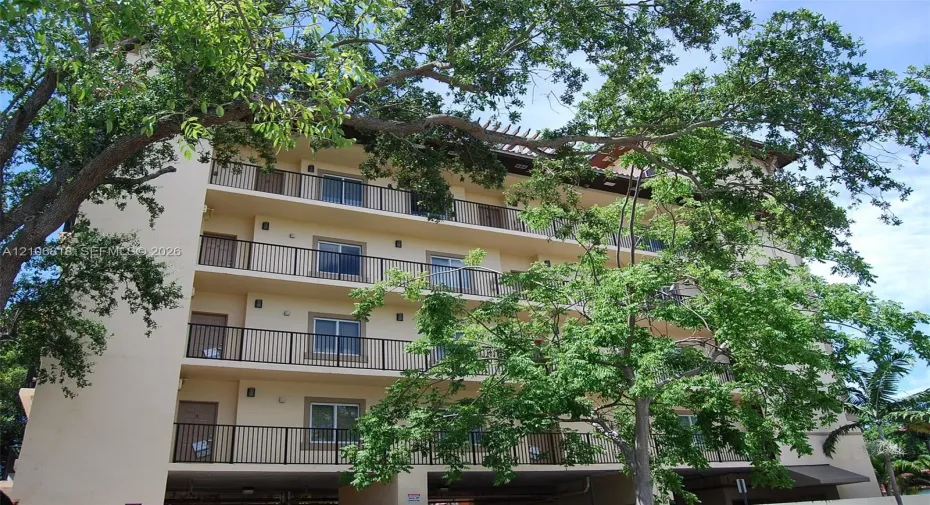Multi-story building exterior featuring stacked private balconies, metal railings, and a covered ground-level parking area
