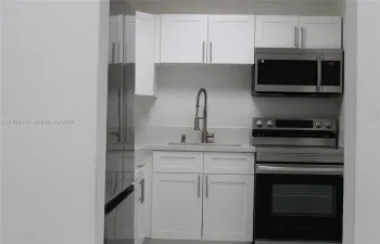 Kitchenette featuring white Shaker-style cabinetry, stainless steel appliances, a stone-composite countertop, and a gooseneck faucet