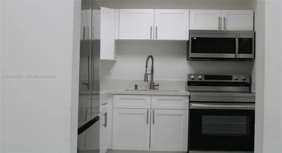 Kitchenette featuring white Shaker-style cabinetry, stainless steel appliances, a stone-composite countertop, and a gooseneck faucet