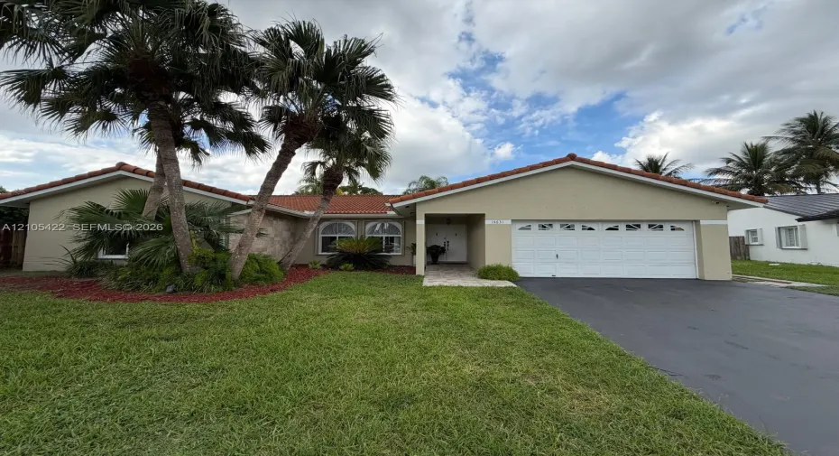 Single-story residence featuring a tile roof, arched windows, an attached two-car garage, stone facade accents, and mature palm landscaping