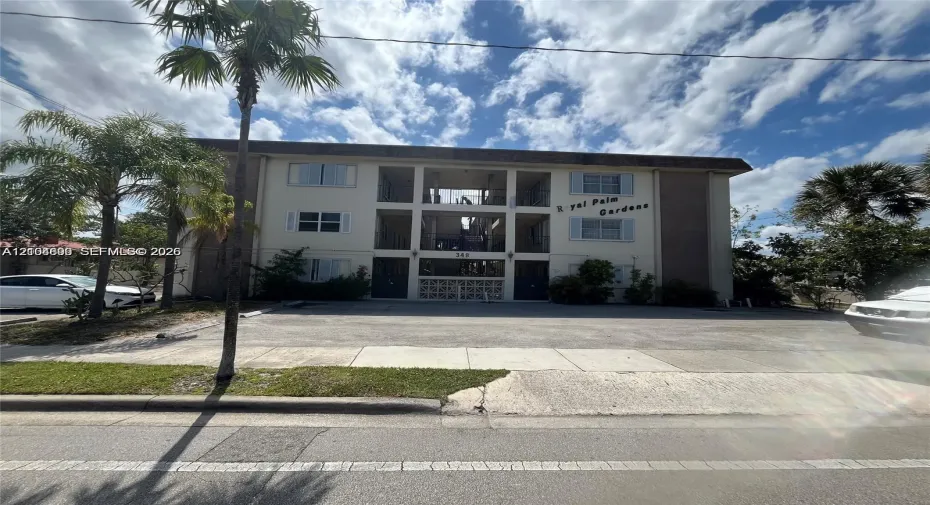 Three-story multi-unit structure featuring a concrete facade, decorative breezeblock accents, exterior stairwell, and surface parking