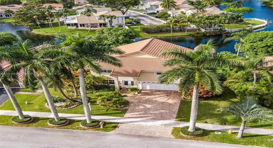 Two-story residence featuring a tile roof, brick-paver driveway, multi-car garage, mature palm landscaping, and waterfront positioning