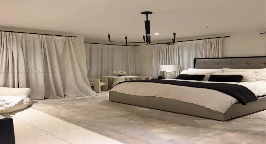 Spacious room featuring light-toned tile flooring, floor-to-ceiling drapery panels on black hardware, and a multi-arm geometric chandelier with a black finish
