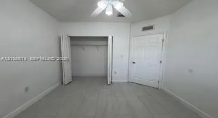 Interior room featuring light-toned tile flooring, a dual-door closet, a six-panel door, and a ceiling fan with integrated lighting