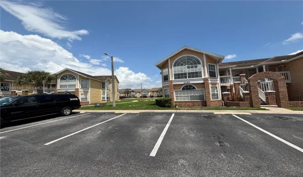 Multi-story exterior featuring tan siding, brick masonry detailing, arched window accents, and railed balconies