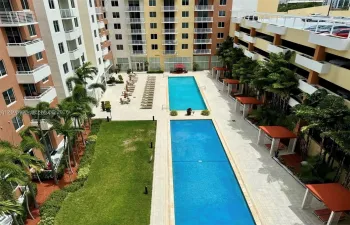 Outdoor amenity area featuring two rectangular swimming pools, stone-paved deck, manicured lawn, and multiple shaded cabanas