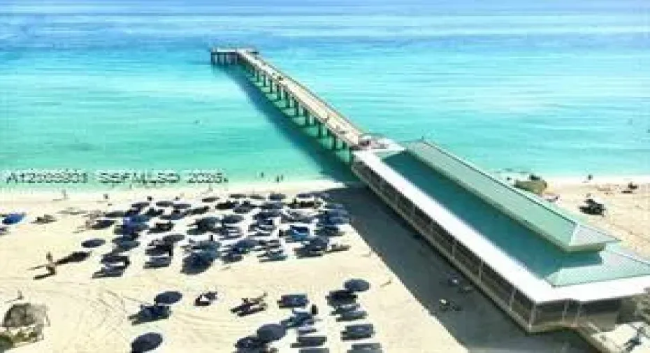 Aerial perspective of a coastal pier with a pitched metal roof, sandy beachfront, and direct ocean access