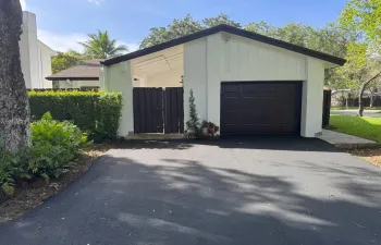 Exterior featuring a paved asphalt driveway, an attached garage with a dark-toned door, a covered entry with wood-slat screening, and low-maintenance landscaping