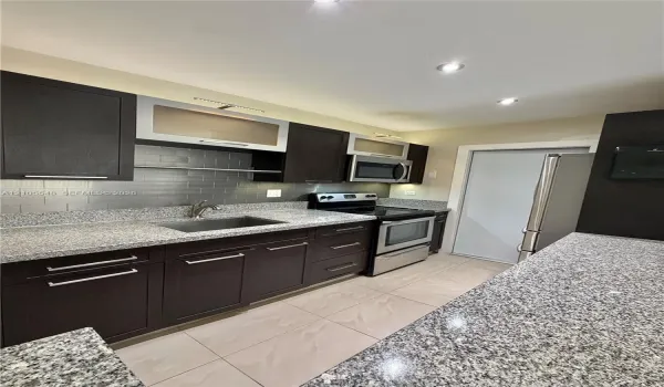 Kitchen featuring modern cabinetry, stone-finish countertops, subway tile backsplash, stainless steel appliances, and large-format tile flooring