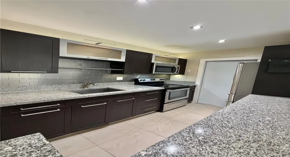 Kitchen featuring modern cabinetry, stone-finish countertops, subway tile backsplash, stainless steel appliances, and large-format tile flooring