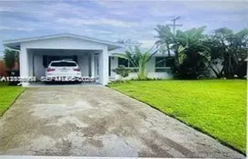 Single-story residence featuring a covered carport, concrete driveway, and established landscaping with mature palm trees