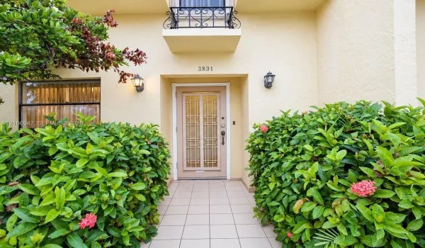 Entryway featuring a decorative metal-grille front door, wrought iron balcony railing, stucco exterior, ceramic tile walkway, and wall-mounted exterior lighting