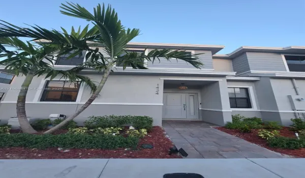 Two-story exterior featuring a gray stucco and horizontal siding facade, paver walkway, recessed entryway, and mature palm trees