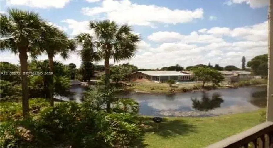 Waterfront property featuring a private canal, mature palm trees, expansive lawn, and single-story masonry residence