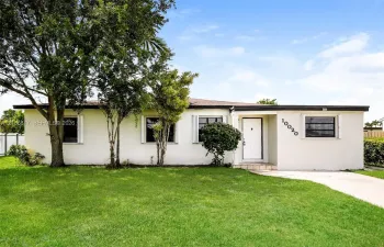 Single-story residence featuring a smooth stucco exterior, low-pitched roofline, horizontal sliding windows with exterior shutters, and a concrete driveway