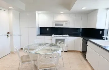 Kitchen featuring white cabinetry, dark countertops, tile flooring, and integrated white appliances