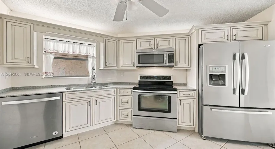 Kitchen featuring light-toned cabinetry, stainless steel appliances, speckled stone-finish countertops, and tile flooring