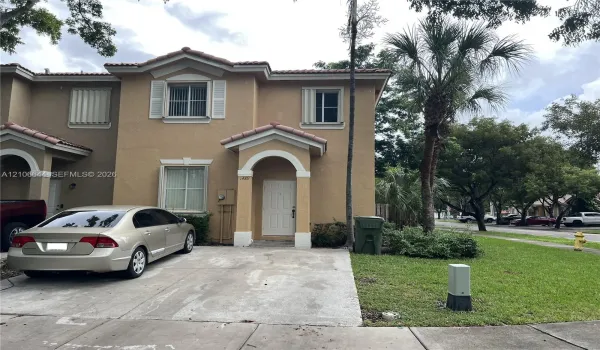 Two-story stucco exterior featuring a covered entryway, decorative arched molding, tiled roof, and an attached concrete driveway