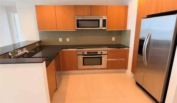 Kitchen featuring flat-panel wood cabinetry, dark stone countertops, stainless steel appliances, and a glass-tile backsplash