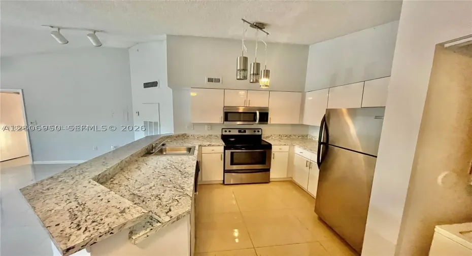 Kitchen featuring a raised breakfast bar with stone-finish countertops, white cabinetry, stainless steel appliances, and multi-light pendant illumination