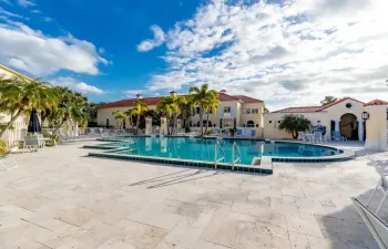 In-ground swimming pool with tile trim, expansive stone paver patio, and mature palm trees