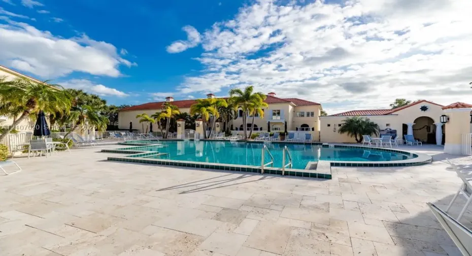 In-ground swimming pool with tile trim, expansive stone paver patio, and mature palm trees