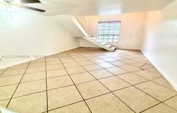 Open-concept space featuring diagonal tile flooring, high ceilings, a window with horizontal blinds, and a staircase with a white metal railing