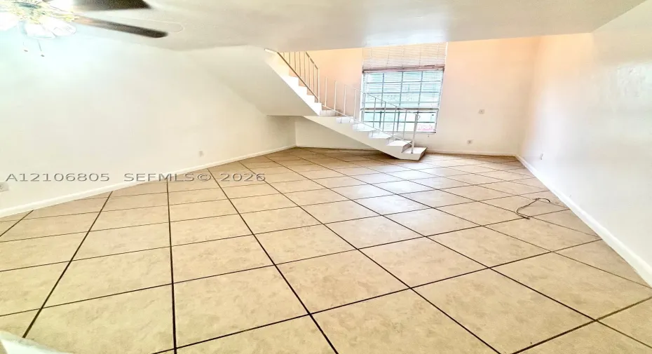 Open-concept space featuring diagonal tile flooring, high ceilings, a window with horizontal blinds, and a staircase with a white metal railing