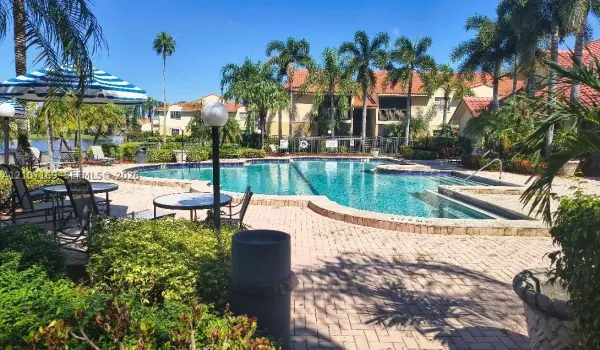 In-ground swimming pool featuring a brick paver deck, integrated spa, and landscaping with mature palm trees