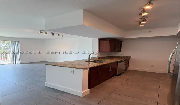 Kitchen featuring wood cabinetry, stone countertops, an undermount stainless steel sink with a high-arch faucet, large-format tile flooring, and multi-directional track lighting