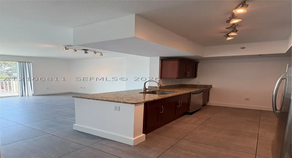 Kitchen featuring wood cabinetry, stone countertops, an undermount stainless steel sink with a high-arch faucet, large-format tile flooring, and multi-directional track lighting