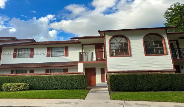 Multi-level exterior featuring a stucco and horizontal siding facade, arched window detailing, a second-story balcony with metal railing, and manicured perimeter hedging